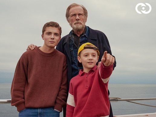 Bill Nighy is with two young boys on a boat, one of the boys is pointing off to the sea.