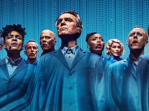 David Byrne stands centrally with his cast all dressed in blue against a blue background.