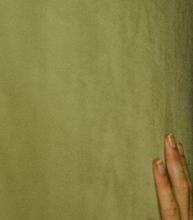 A woman is pressed up against a yellow wall. She is gasping in fear.
