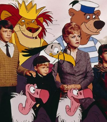 A young woman and three children are gathered with some animated characters includign a lion, a bear and a vulture.
