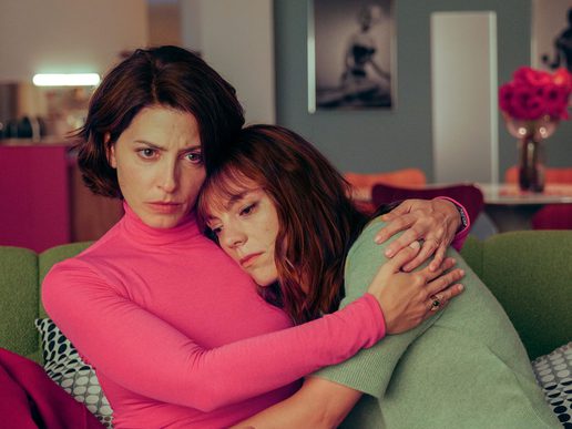 Two women are sat on a sofa with one hugging the other.