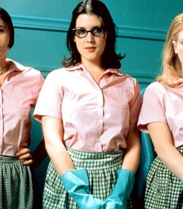 Three women in pink tops with rubber gloves are stood in a line.