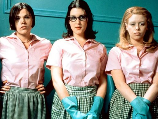 Three women in pink tops with rubber gloves are stood in a line.