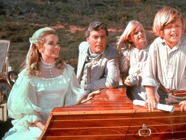 A woman, a Man and two children are sat atop a wooden panelled car.