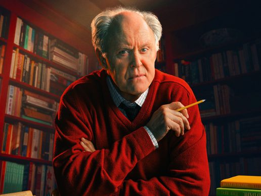 Actor John Lithgow appears in a red jumper in a writing study holding a pencil.