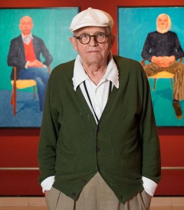 David Hockney stands infront of two of his paintings in an exhibition.