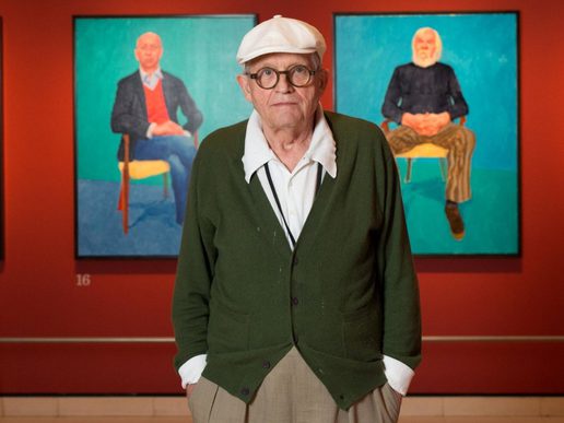 David Hockney stands infront of two of his paintings in an exhibition.