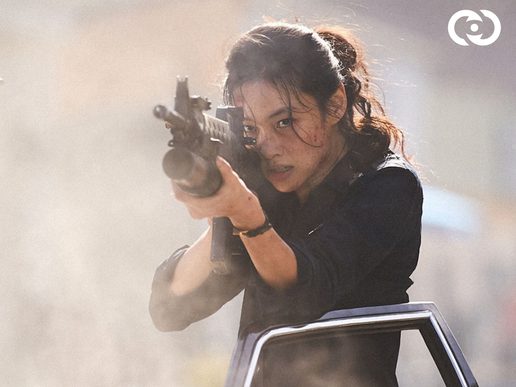 A woman is leaning out of a car with a huge gun aimed at something off screen.