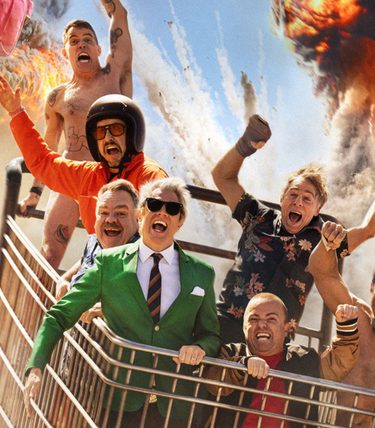 The Jackass gang are all in a giant shopping trolley with explosions going off behind them.
