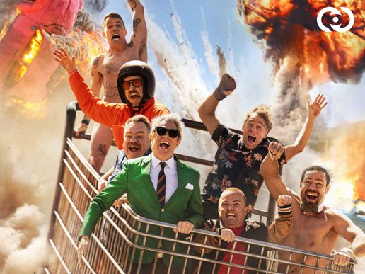 The Jackass gang are all in a giant shopping trolley with explosions going off behind them.