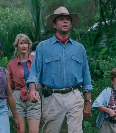 A man in a blue shirt and straw hat is standing with two young children and a woman in a forest background.