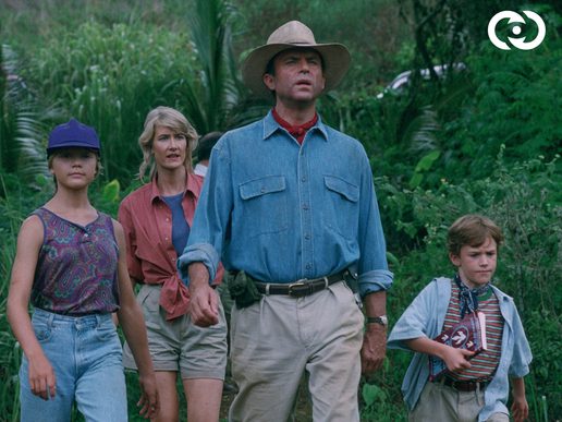 A man in a blue shirt and straw hat is standing with two young children and a woman in a forest background.
