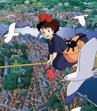 A young witch is flying on a brromstick over a town. She has a cat and is flying alongside birds.