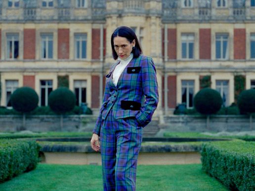 An aristocratic lady in a striking blue suit is outside a stately manor.