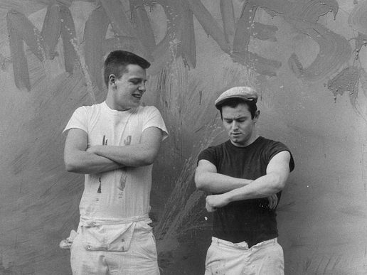Two members of Madness in a black and white photo against aa wall where they have painted 'Madness'.