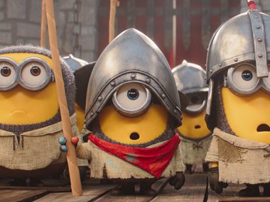Three of the yellow minions characters are standing in a line, they are wearing medieval armour and carrying spears.