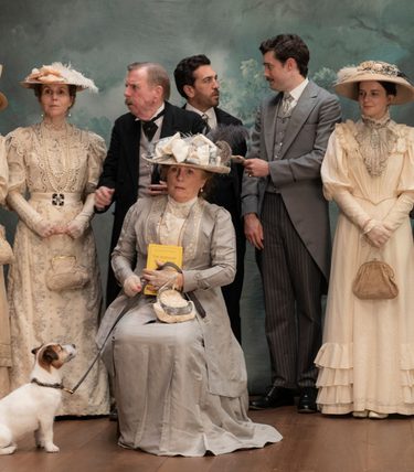 An ensemble cast in period dress are posing for a photograph.