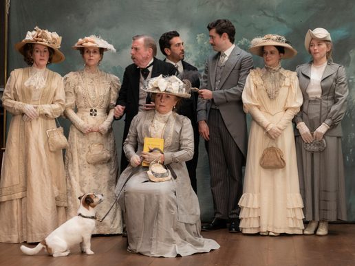 An ensemble cast in period dress are posing for a photograph.