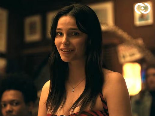 A woman with long dark hari is looking at the camera. She is in a reastaurant with onlookers behind her.