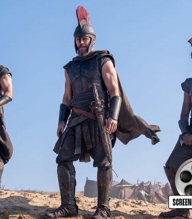 Three warriors in armour and helmets stand upon a cliff top.