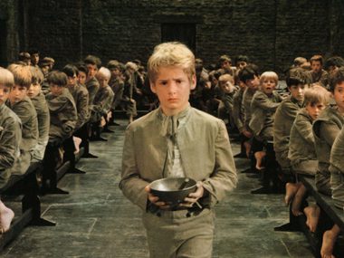 A young boystands among a group of other boys. He is holding a bowl.