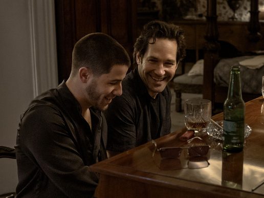 Paul Rudd and Nick Jonas are both sat at a piano and smiling. There are glasses of whickey on top.