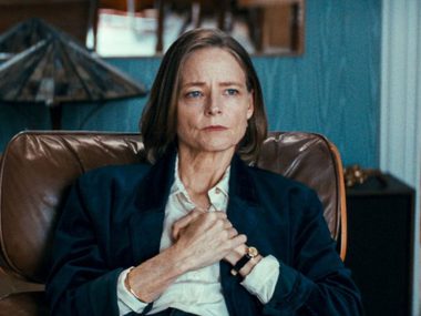 Jodie Foster is sat in a leather chair with her hands crossed across her front.