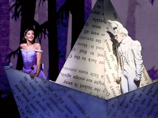 A young female dancer is emerging from a giant story book shaped into a boat. A man in white is staring at her.