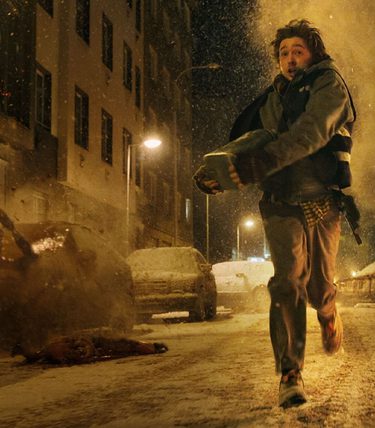 A man is running down a dark street with snowy cars behind him.