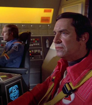 Martin Landau is sat in a spacehip looking toward the controls.