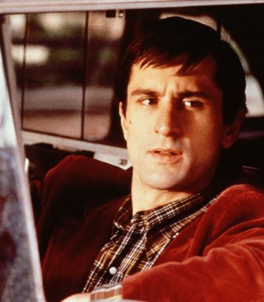 Robert De Niro is sat at the wheel of a taxi cab looking outwards.
