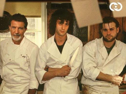 Three men in Chefs whites are standing in a line posing for a photo. An older one looks smart while two younger men look disheveled.