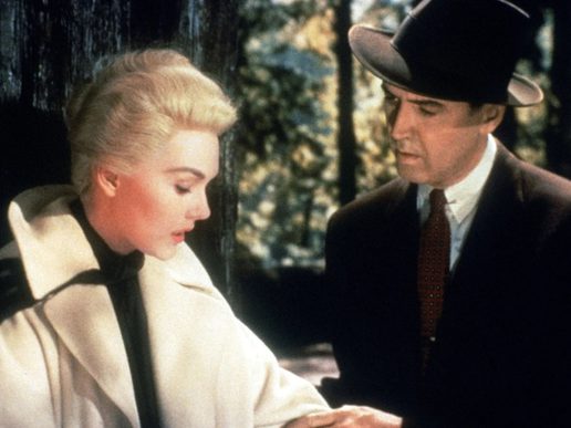 A man in a hat and a woman in a stiking white jacket are outside in a redwood forest.