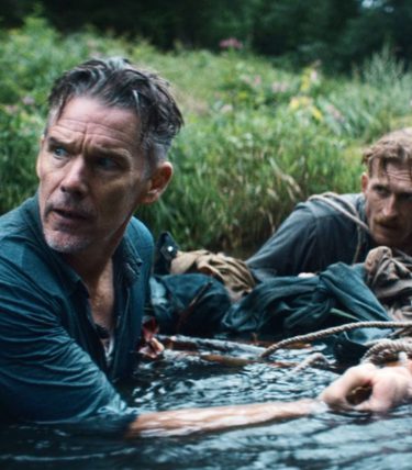 Ethan Hawke is chest high in a river, pulling something along with another man.