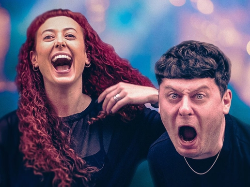 Two performers pose closely together against a blurred, colourful background; one with long red hair laughs widely, while the other pulls a shocked, open-mouthed expression, creating a bold, exaggerated contrast in mood.