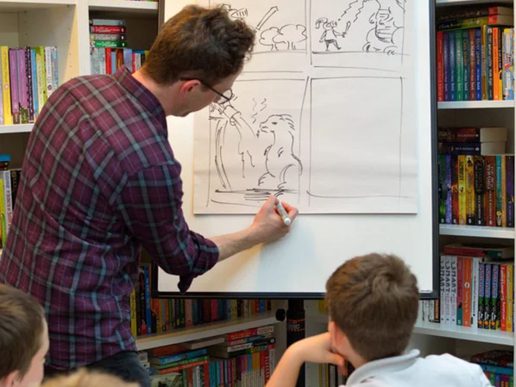 Person drawing a comic strip on a whiteboard while children watch, with bookshelves filled with colourful books in the background.