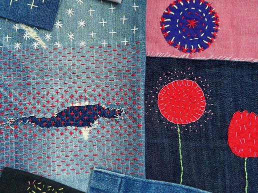 Patchwork of denim and fabric pieces decorated with colourful visible mending and embroidery, including stitched patterns, repaired tears, and appliqué designs in red, blue, and pink.