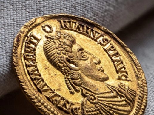 Close-up of an ancient gold Roman coin featuring the profile of a woman wearing an elaborate hairstyle, surrounded by Latin lettering.