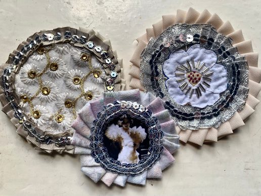 Three handmade circular textile corsages decorated with layered fabric, sequins, metallic embroidery and beads, including floral and photographic designs.