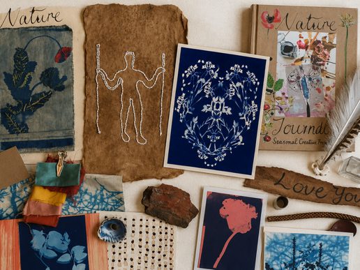 A flat lay of handmade nature-inspired artwork and creative materials arranged on a white surface. The display includes botanical cyanotype prints, stitched paper art, fabric samples, pressed plant designs, a handmade nature journal, feathers, natural pigments, bark, shells and other found objects, creating a colourful collage celebrating creativity and the natural world.