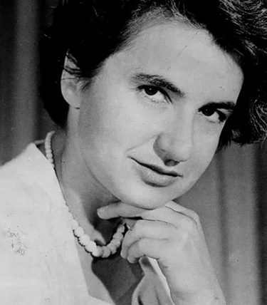Black-and-white portrait of Rosalind Franklin, the pioneering British chemist and X-ray crystallographer known for her vital role in the discovery of DNA's double helix structure. She gazes confidently at the camera with her chin resting thoughtfully on her hand. Her short, wavy hair is styled neatly, and she wears a light blouse and a simple beaded necklace. The background is softly lit, placing focus on her composed expression and scientific legacy.