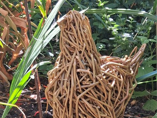 Woven willow sculpture of a hen standing among green plants in a sunlit garden.