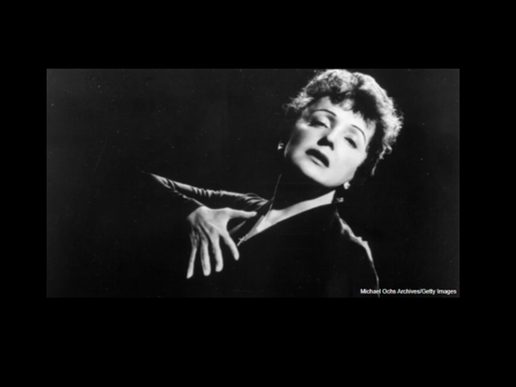Black-and-white portrait of singer Édith Piaf in a dramatic performance pose. Wearing a dark dress against a black background, she tilts her head back with eyes half closed and one hand raised to her chest, capturing the emotion and intensity of her stage presence.