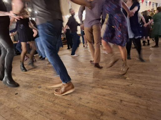 Blurred motion of people dancing on a wooden floor, capturing energetic footwork and movement during a lively social dance.