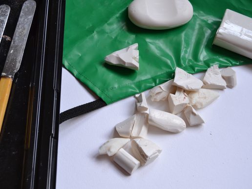 Close-up of white soap pieces being carved on a green cutting mat, with carving knives and a partially shaped piece of soap.