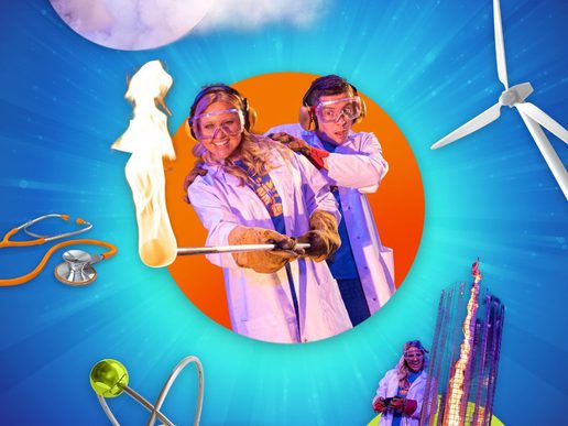 Two performers in lab coats, goggles, and gloves hold a flaming test tube on a metal rod, smiling and reacting with excitement, against a bright blue background with a large orange circle and science-themed graphics including a stethoscope and a wind turbine.
